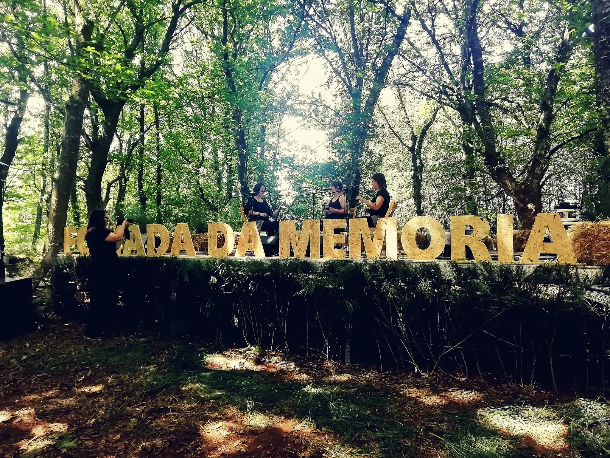O letreiro «Foliada da Memoria» nun souto, cos músicos ao fondo