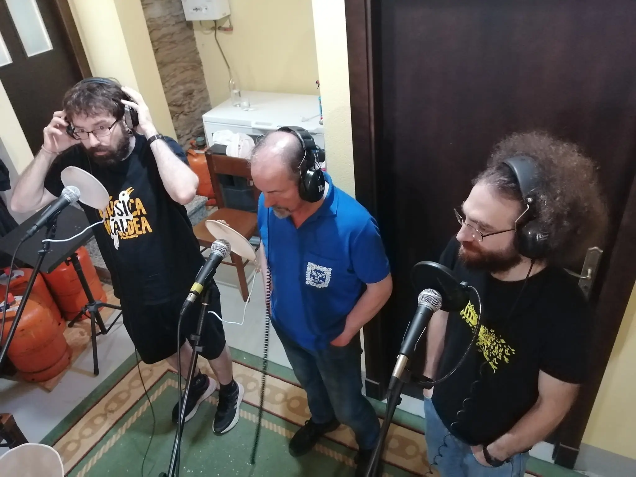 Tres homes con auriculares diante dos micrófonos