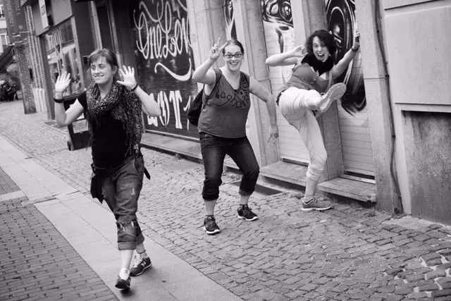Tres mulleres bailan e dan patadas ao aire nunha rúa, en branco e negro