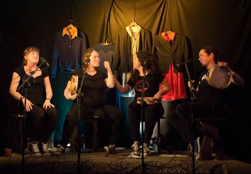 Catro músicas tocan sentadas nun escenario, con roupa colgada detrás
